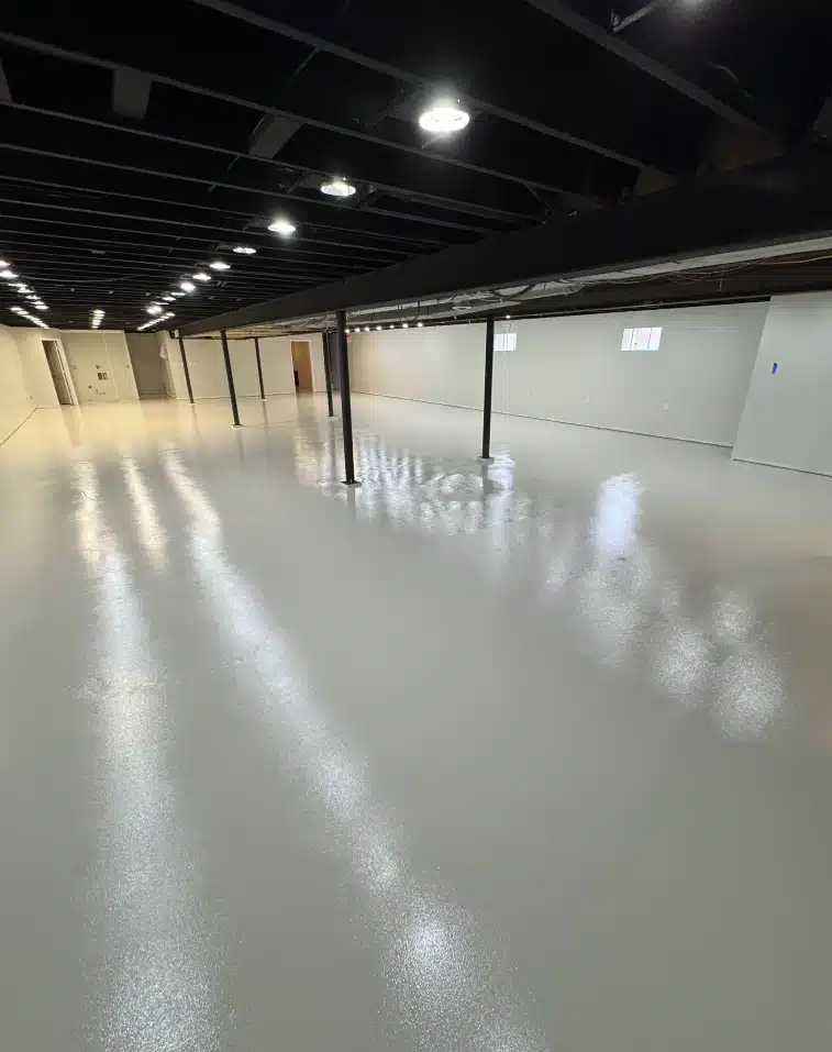 Basement epoxy flooring with a glossy light gray finish, white walls and exposed black ceiling beams.