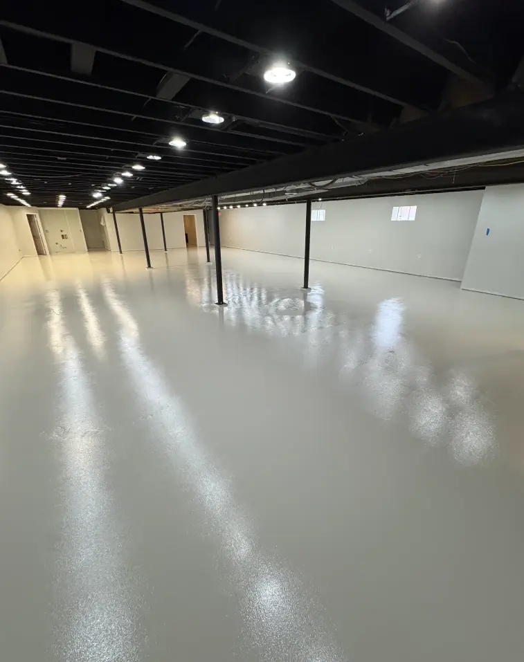 Glossy light gray epoxy floor in a finished basement with exposed ceiling beams