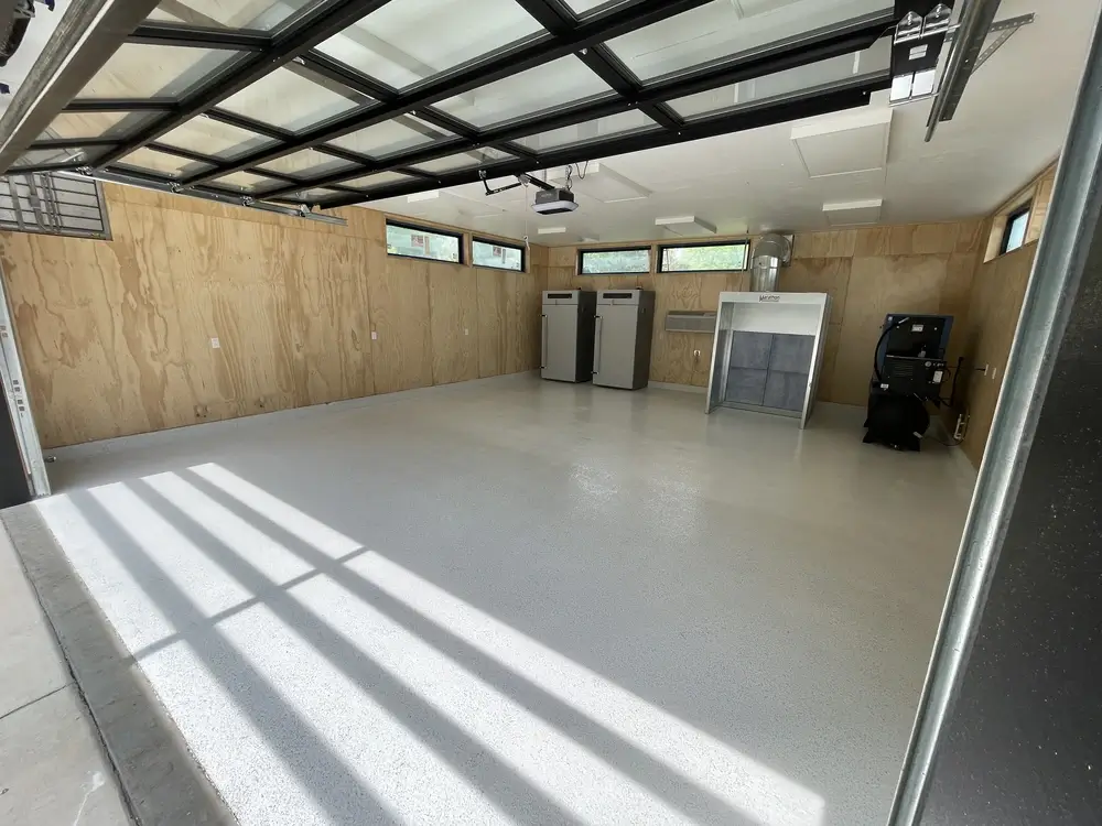 Light gray garage floor epoxy with a speckled finish in a wood-paneled residential garage.