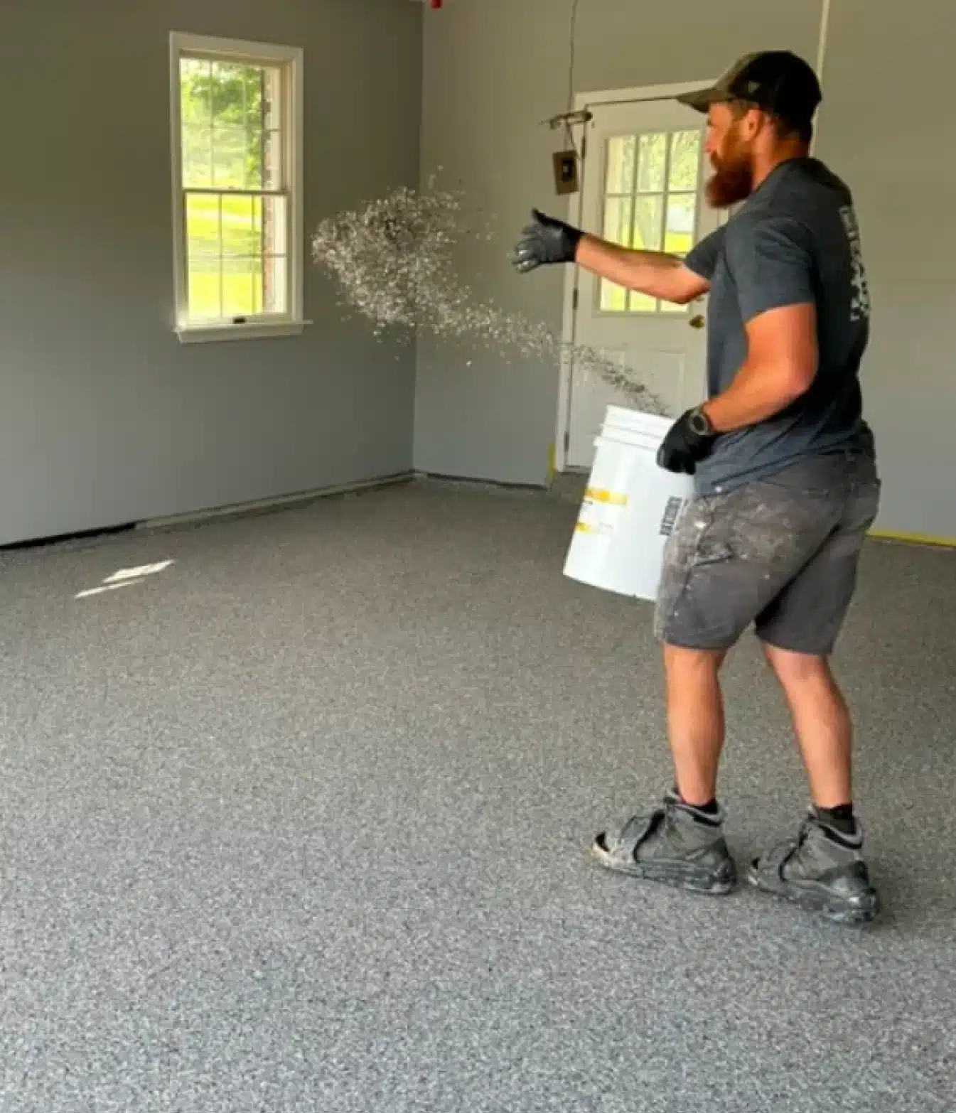 Installer broadcasting decorative flakes onto a gray epoxy garage floor