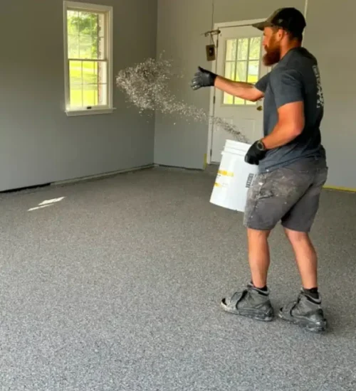 Installer broadcasting decorative flakes onto a gray epoxy garage floor