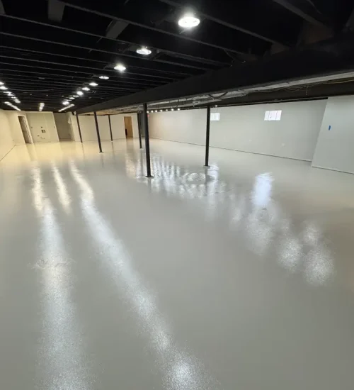 Glossy light gray epoxy floor in a finished basement with exposed ceiling beams