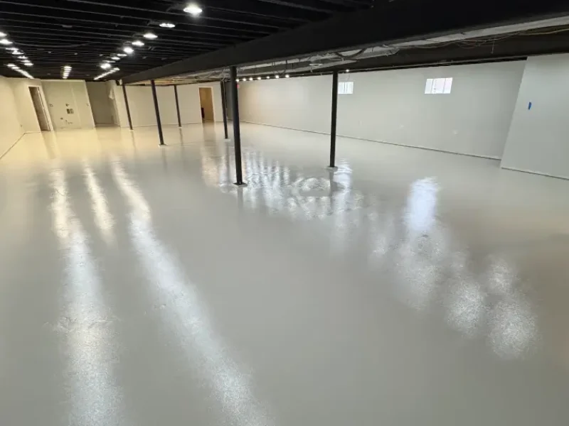 Glossy light gray epoxy floor in a finished basement with exposed ceiling beams